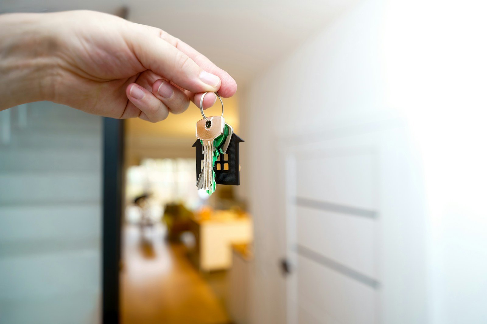 A hand holding out house keys at the front door of a home